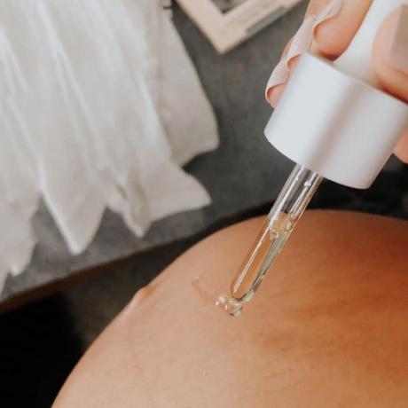 Крупним планом масло для тіла з крапельниці капає на вагітний живіт.