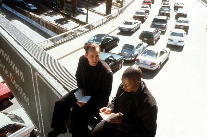 Scenoje iš filmo „Angelų miestas“, 1998 m., Nicolas Cage'as ir Andre Braugheris sėdi ant greitkelio viaduko ženklo, po jais intensyvus eismas.