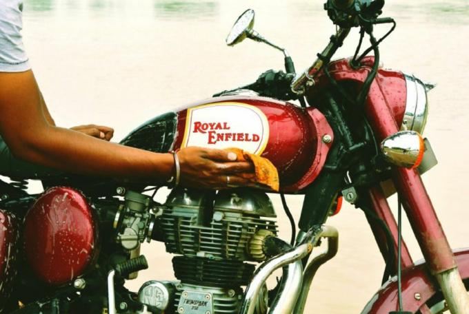 Detail seseorang mengeringkan sepeda motor basah dengan kain oranye.