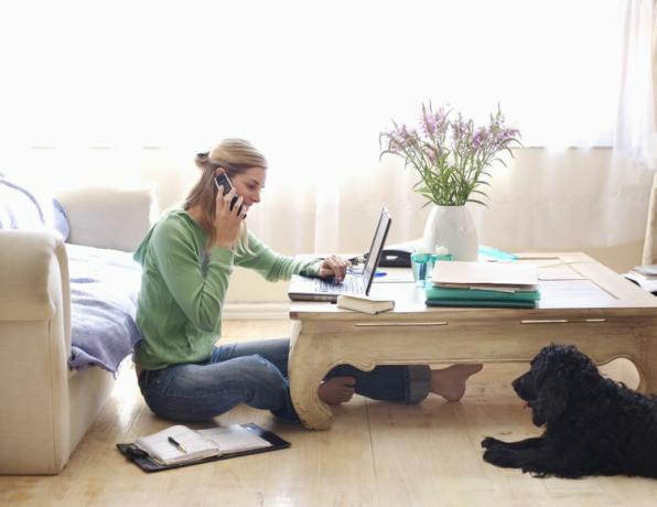 Femme parlant au téléphone tout en utilisant son ordinateur à la maison