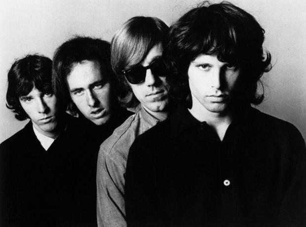 Črno-bela promocijska fotografija The Doors s pevcem Jimom Morrisonom spredaj.