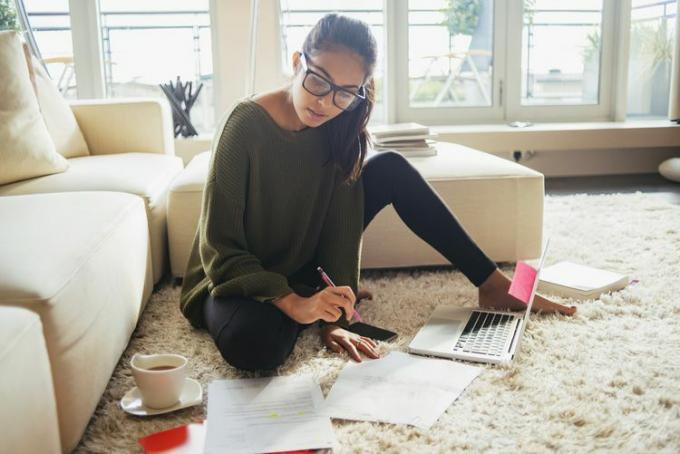 Una joven escribe un resumen en una computadora portátil rodeada de sus notas e investigaciones. Aprende a escribir un resumen aquí.
