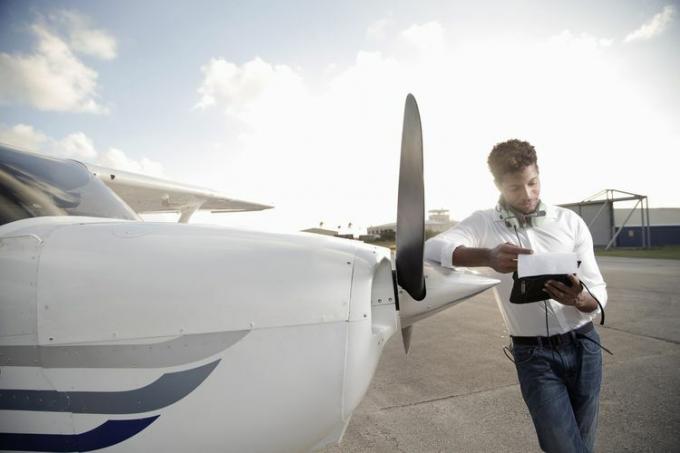 Młody pilot stojący przy swoim samolocie i patrzący na papier