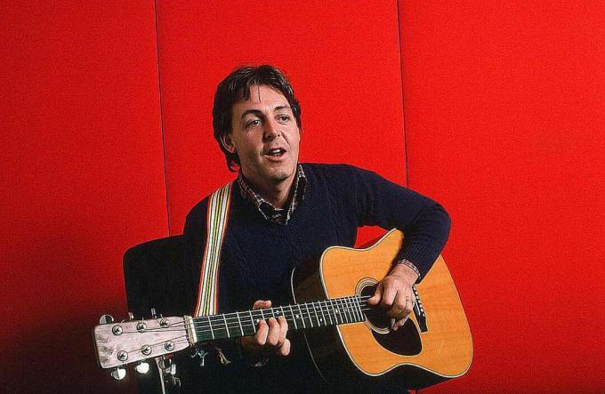 Paul McCartney în timp ce cântă la chitară acustică pe un fundal roșu, 7 octombrie 1984.