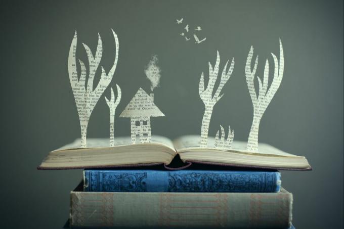 Открытая книга с вырезками из бумаги, появляющаяся в форме дома и нескольких деревьев.