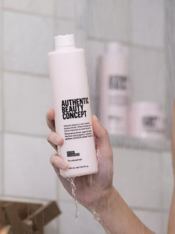 En hand håller upp produkten i en duschdimma.