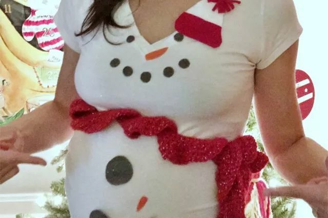 Seorang wanita hamil mengenakan sweter jelek manusia salju